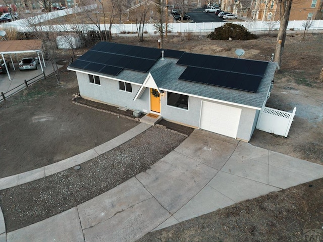 single story home with roof with shingles, stucco siding, concrete driveway, roof mounted solar panels, and fence