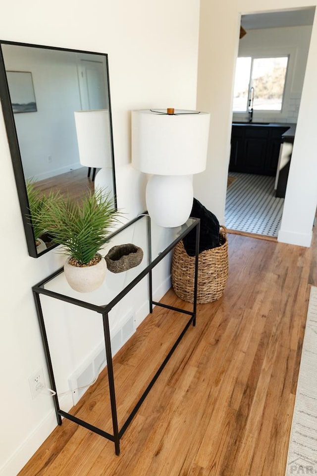 corridor with light wood-style floors, a sink, and baseboards