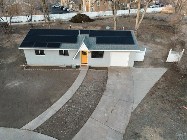 ranch-style home featuring stucco siding, a shingled roof, concrete driveway, roof mounted solar panels, and fence