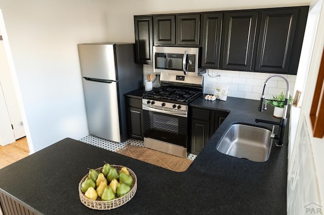 kitchen featuring dark countertops, decorative backsplash, appliances with stainless steel finishes, a sink, and dark cabinets