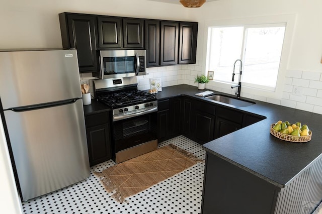 kitchen featuring dark countertops, appliances with stainless steel finishes, backsplash, and a sink