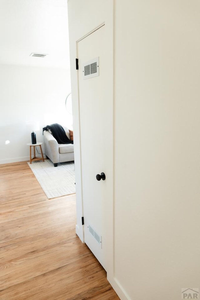 hallway with light wood-style floors, visible vents, and baseboards