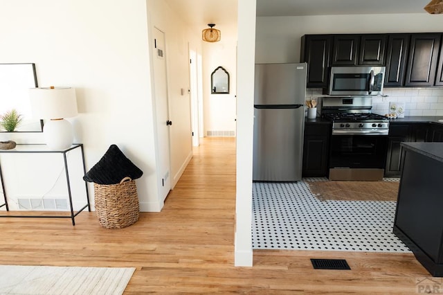 kitchen featuring light wood finished floors, tasteful backsplash, dark countertops, appliances with stainless steel finishes, and dark cabinets