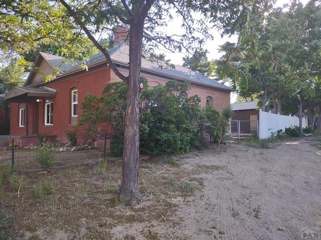 view of property exterior featuring brick siding, fence, and a chimney