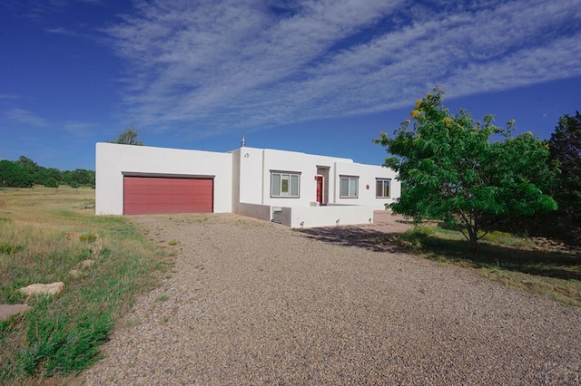 view of front facade featuring an attached garage, gravel driveway, and stucco siding