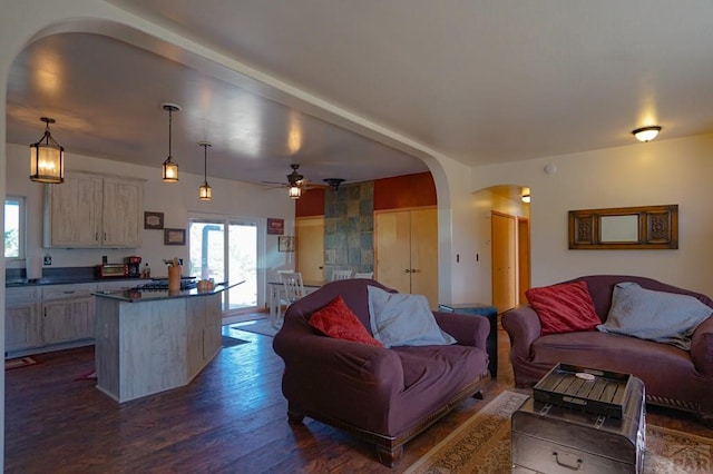 living area with a ceiling fan, arched walkways, and dark wood-style flooring