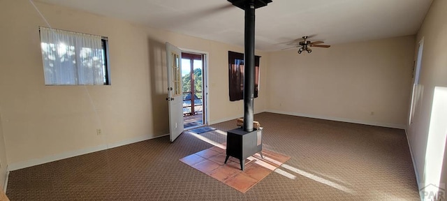 interior space featuring a wood stove, ceiling fan, and baseboards