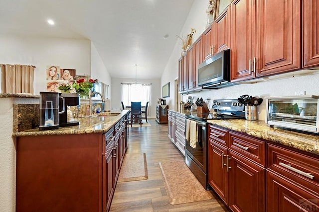 kitchen with stainless steel appliances, a sink, light wood-style floors, dark brown cabinets, and decorative light fixtures