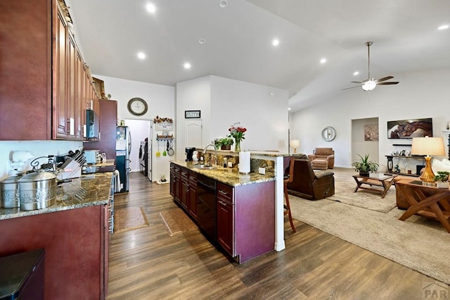 kitchen featuring black dishwasher, open floor plan, a sink, light stone countertops, and a kitchen bar