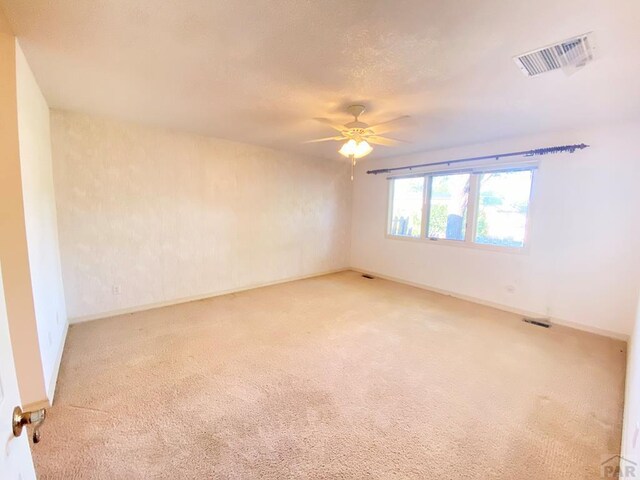 empty room with a ceiling fan, light colored carpet, visible vents, and baseboards