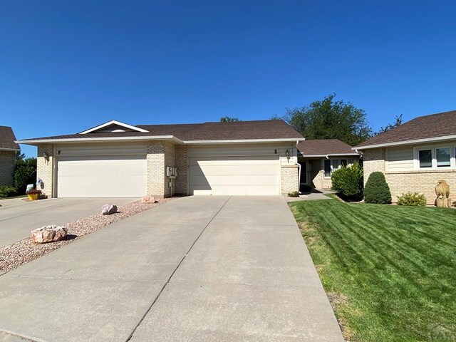 ranch-style house with driveway, brick siding, an attached garage, and a front yard