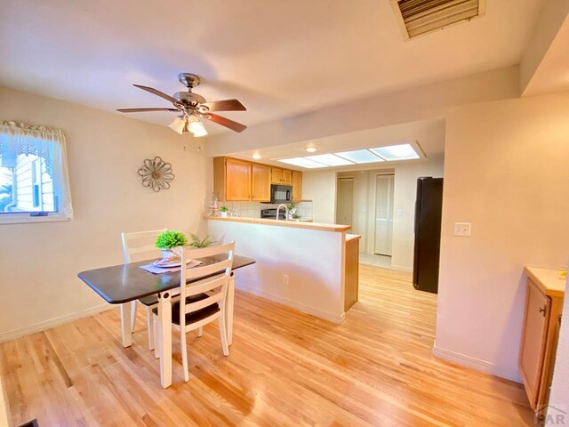 kitchen featuring visible vents, light countertops, light wood-style flooring, a peninsula, and black appliances