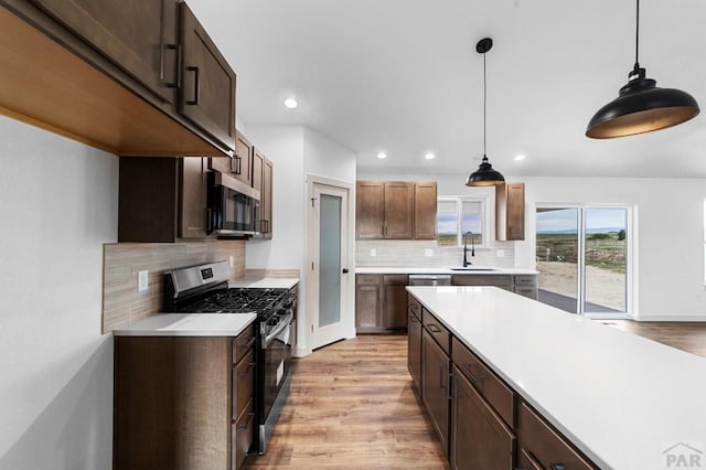 kitchen with light wood finished floors, a sink, tasteful backsplash, light countertops, and appliances with stainless steel finishes