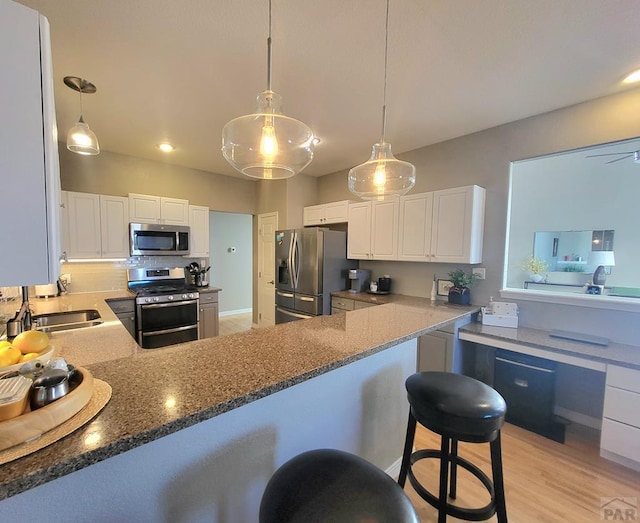 kitchen featuring appliances with stainless steel finishes, white cabinetry, a peninsula, and a kitchen bar