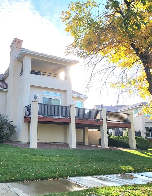 view of front of home with a chimney, a front yard, a balcony, and stucco siding