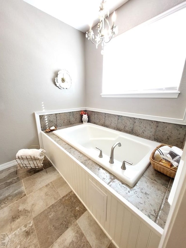 bathroom featuring stone finish floor, a garden tub, and an inviting chandelier