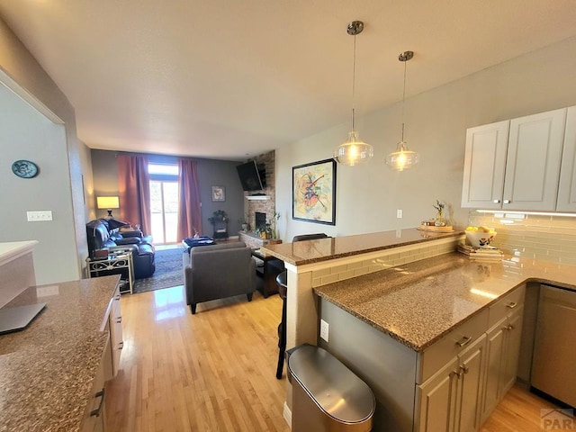 kitchen with stone counters, open floor plan, a peninsula, decorative backsplash, and light wood finished floors