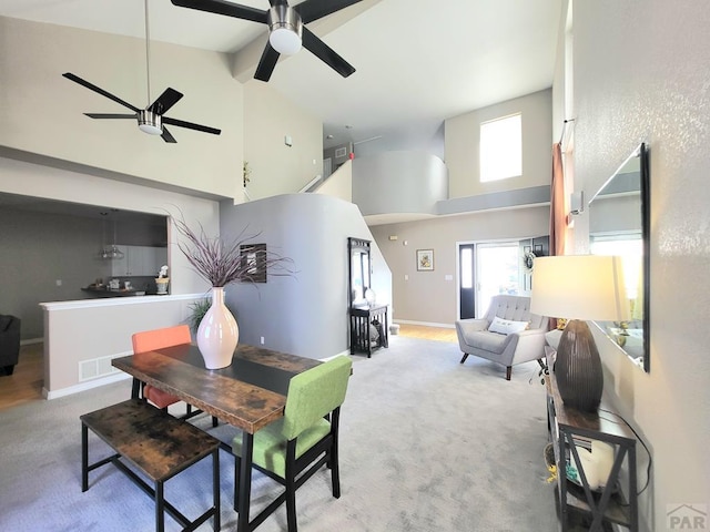 dining space featuring visible vents, baseboards, light colored carpet, ceiling fan, and a high ceiling