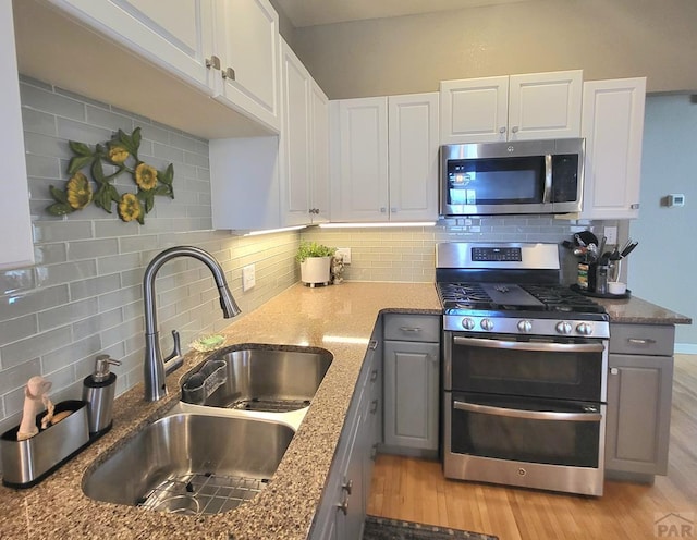 kitchen featuring gray cabinetry, stainless steel appliances, a sink, white cabinetry, and light wood-type flooring