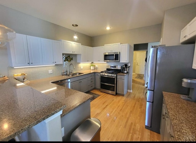 kitchen featuring a sink, a peninsula, light wood finished floors, stainless steel appliances, and decorative backsplash