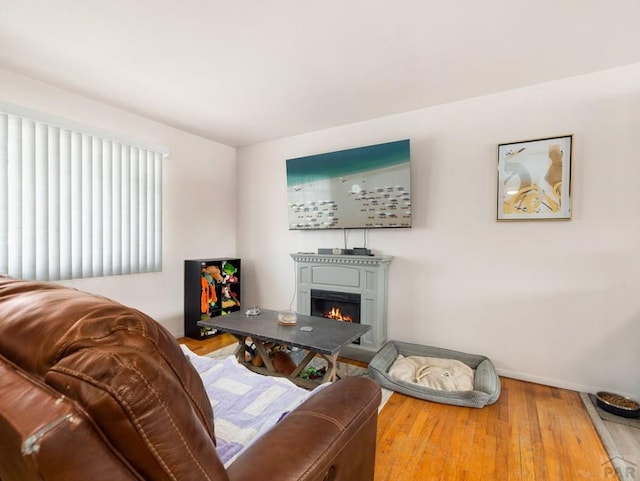 living room with a warm lit fireplace, baseboards, and wood finished floors