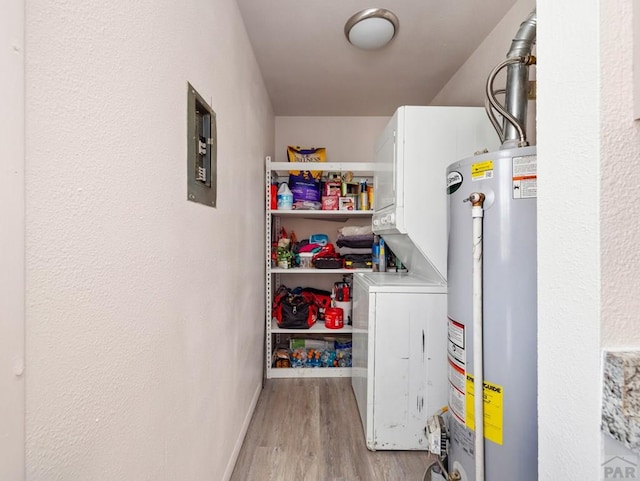 clothes washing area featuring stacked washer and clothes dryer, water heater, light wood-style flooring, laundry area, and baseboards