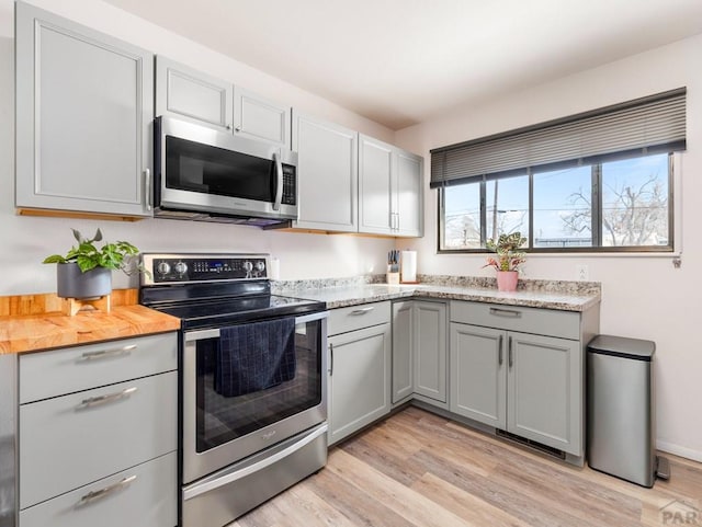 kitchen featuring appliances with stainless steel finishes, light wood-type flooring, gray cabinets, and light stone countertops