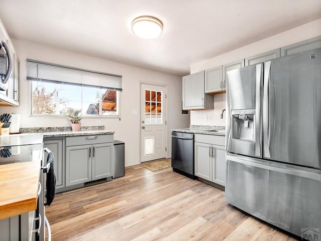 kitchen with light wood-style flooring, gray cabinetry, stainless steel appliances, a sink, and light stone countertops