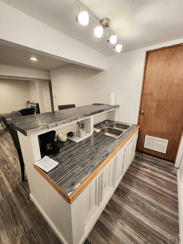 interior space with dark wood finished floors, tile counters, visible vents, white cabinets, and a sink