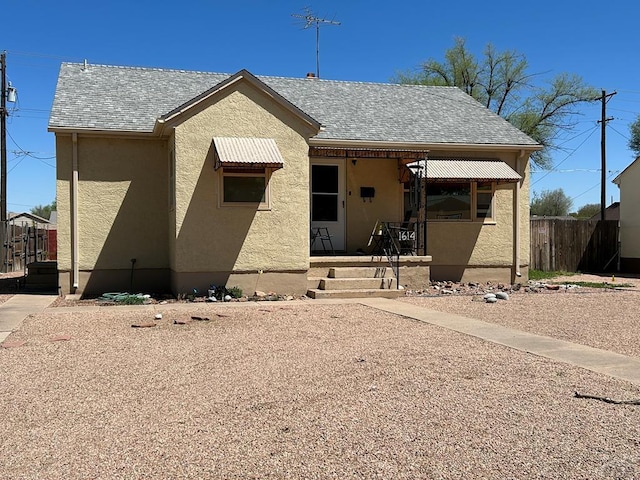 view of front of property featuring a shingled roof, fence, and stucco siding