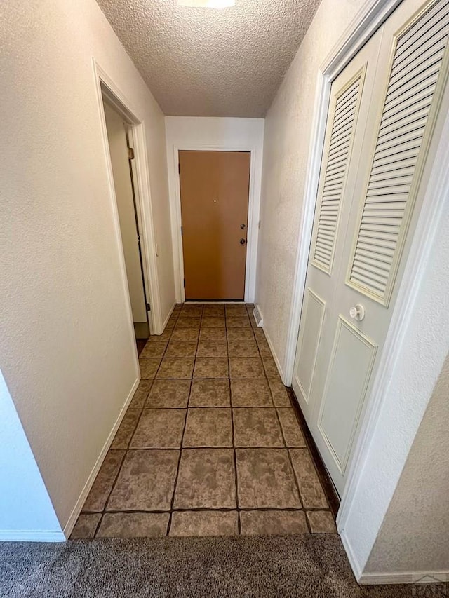 hall featuring baseboards, a textured ceiling, a textured wall, and tile patterned flooring