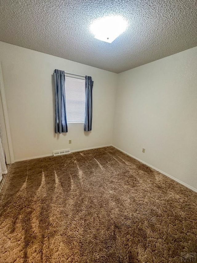 spare room featuring baseboards, visible vents, carpet, and a textured ceiling
