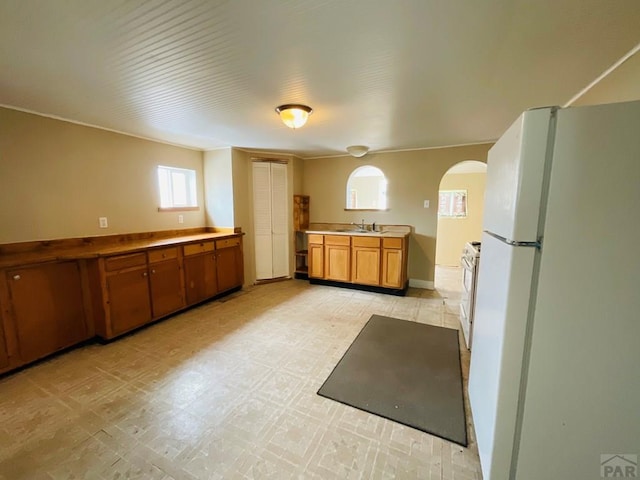 kitchen with arched walkways, white appliances, a sink, brown cabinets, and light floors