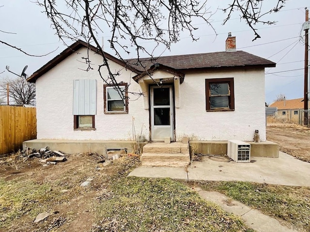 view of front of house featuring a patio, a chimney, stucco siding, a shingled roof, and fence