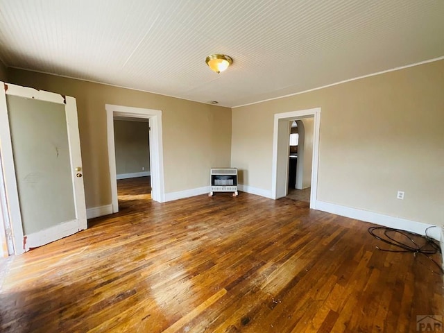 empty room with baseboards, heating unit, and wood finished floors