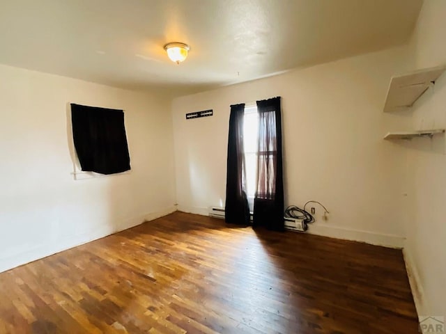 empty room featuring baseboard heating and dark wood finished floors