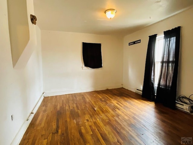 unfurnished room featuring dark wood-style floors, a baseboard heating unit, and baseboards