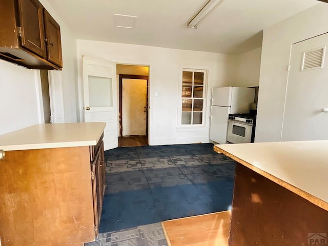 kitchen featuring light countertops, freestanding refrigerator, brown cabinetry, and visible vents