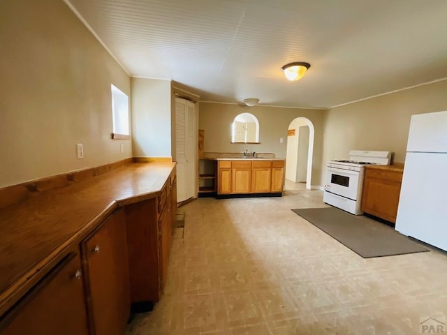 kitchen featuring arched walkways, white appliances, brown cabinetry, and a sink