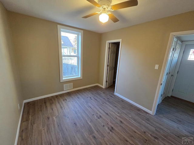 spare room with dark wood-type flooring, visible vents, and baseboards