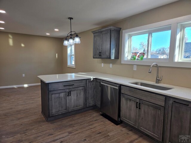 kitchen featuring a peninsula, a sink, light countertops, stainless steel dishwasher, and dark wood-style floors