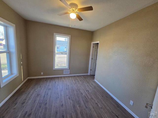 empty room with dark wood-style floors, plenty of natural light, a ceiling fan, and baseboards