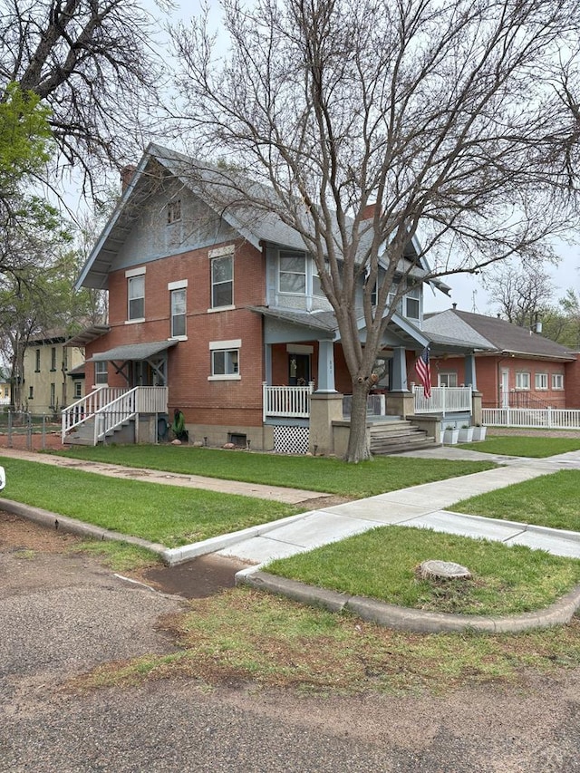 view of front of home with a front lawn, brick siding, covered porch, and a chimney