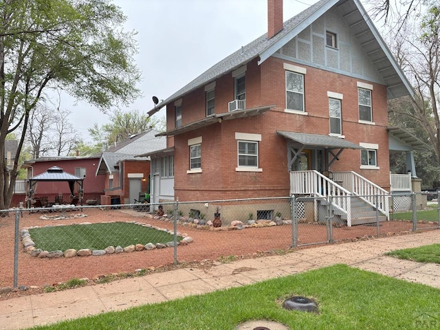 view of front of house featuring fence private yard, a gazebo, a chimney, a shingled roof, and brick siding