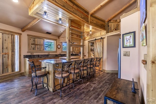 kitchen featuring dark wood-style flooring, dark countertops, a barn door, and a kitchen breakfast bar