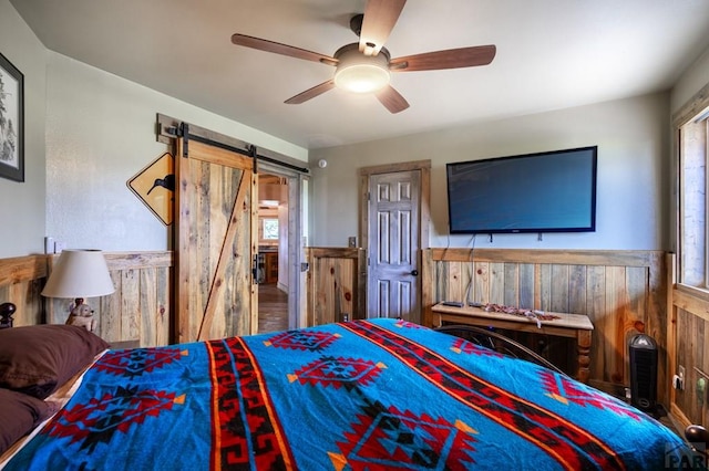 bedroom with a barn door, wainscoting, wood walls, and a ceiling fan