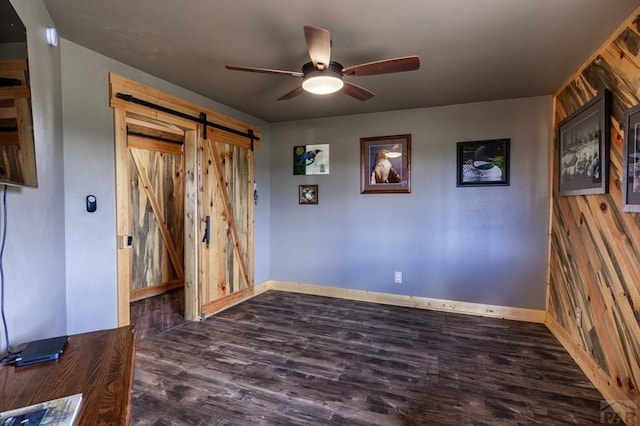 unfurnished room featuring a barn door, ceiling fan, wood finished floors, and baseboards