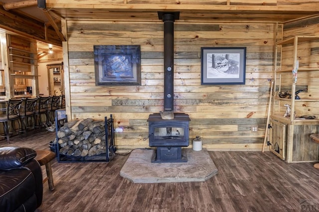 living room with wooden walls, a wood stove, wood finished floors, and beam ceiling