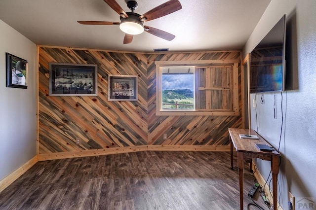 unfurnished office with wooden walls, wood finished floors, baseboards, and a ceiling fan