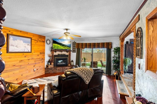 living area featuring a large fireplace, a textured ceiling, dark wood finished floors, and a ceiling fan